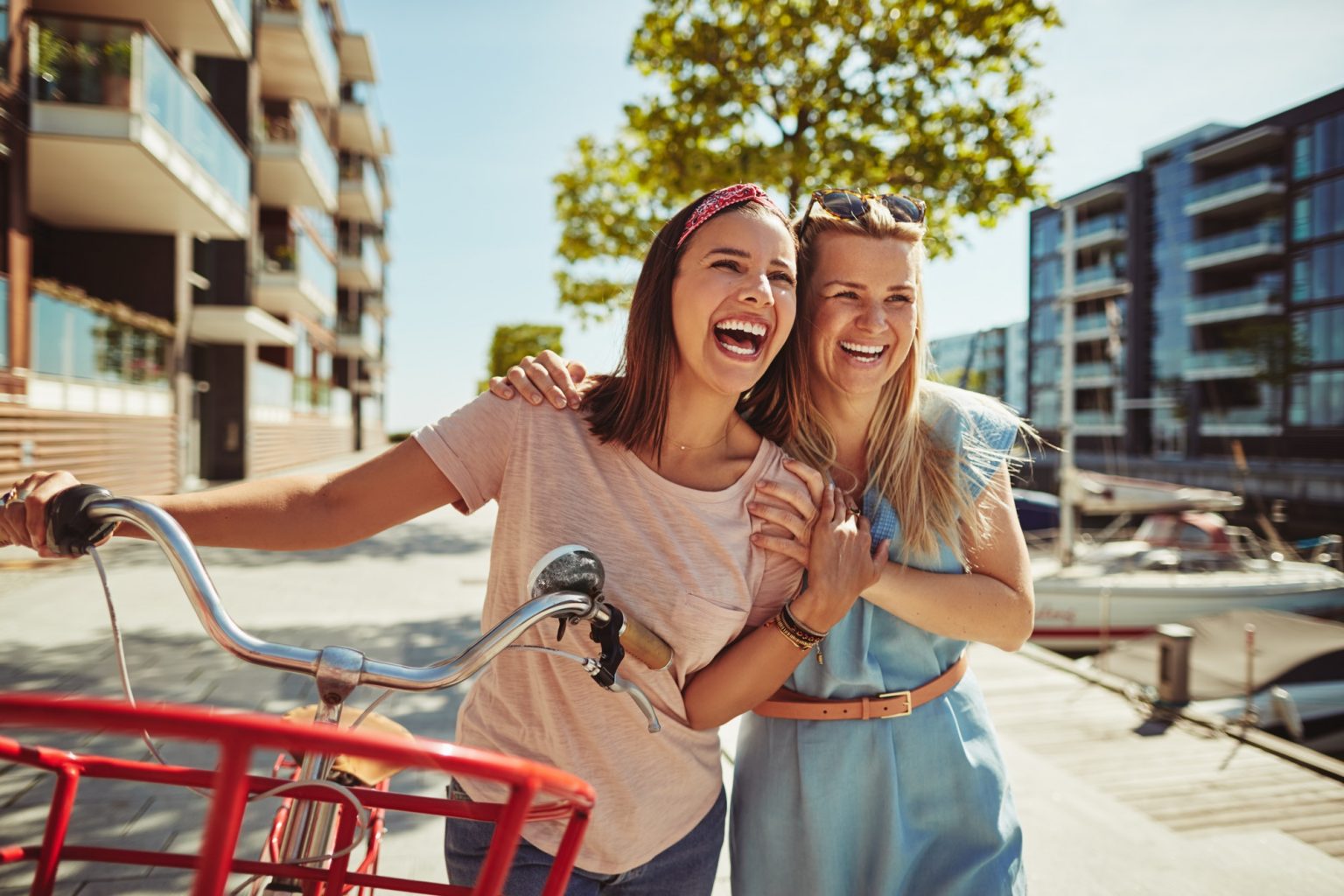 laughing female friends walking with a bicycle through the city