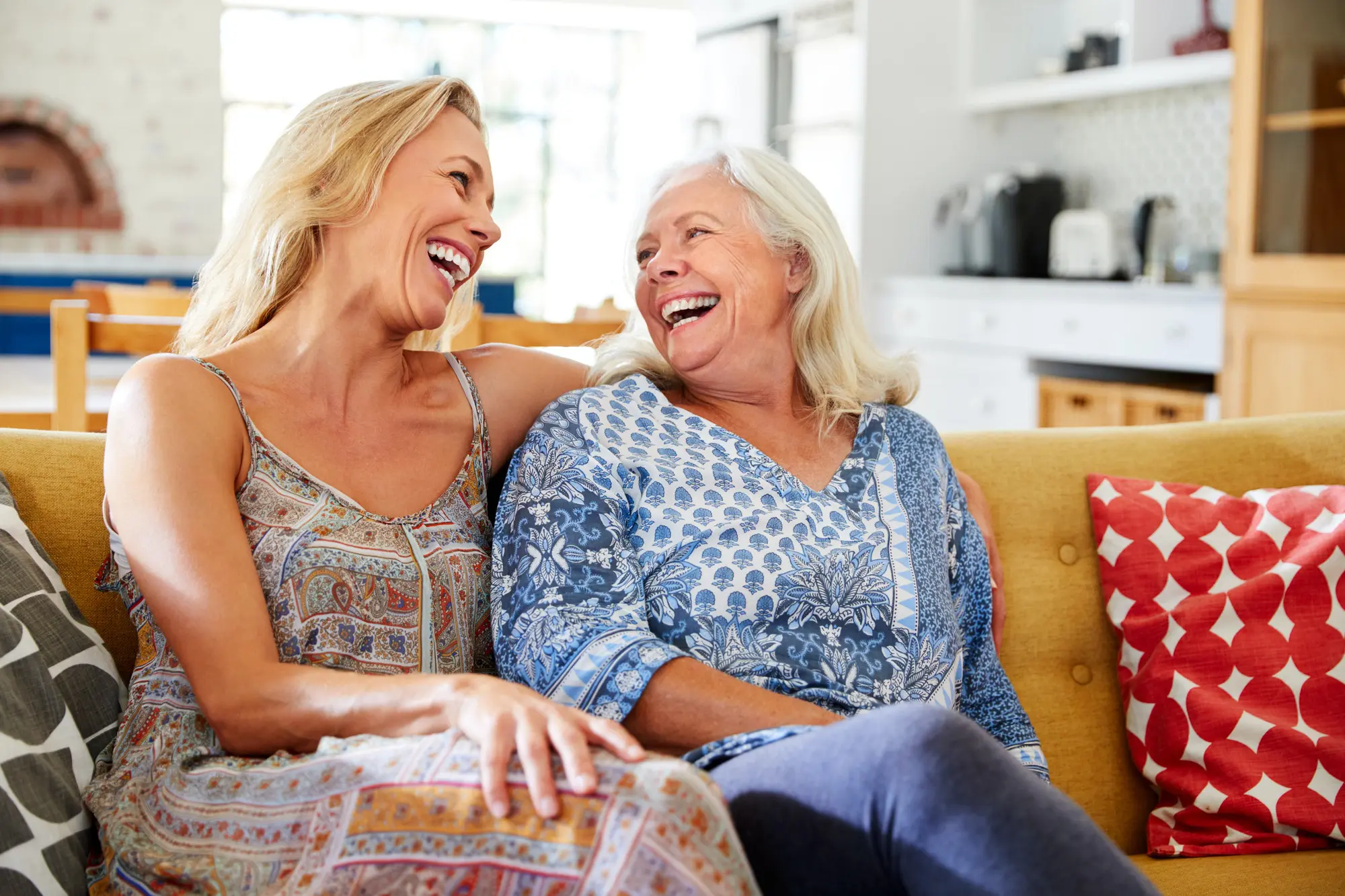 smiling mother with adult daughter relaxing on sofa at home