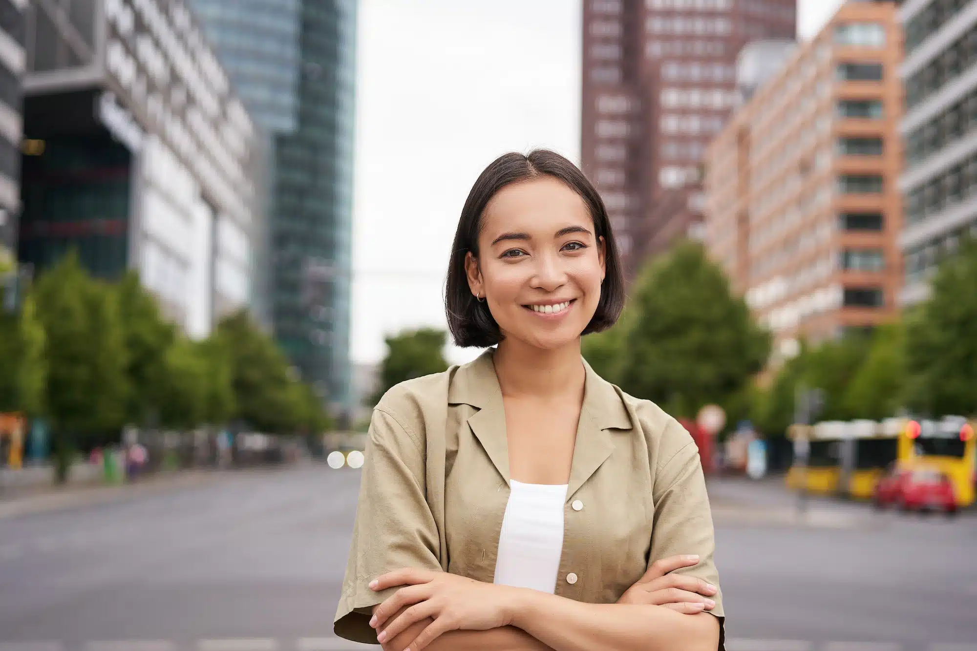 Urban people. Young happy asian girl cross arms on chest, posing on busy city street, smiling with